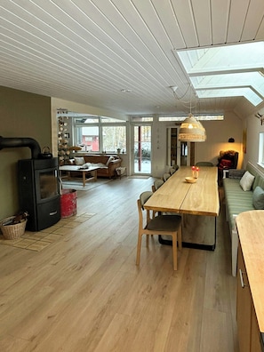 A spacious living area with a wooden dining table, a sofa, and a large window. - Hidden gem by Thy National Park (Bedsted)