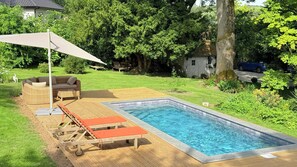 A rectangular swimming pool with a wooden deck, a wicker sofa, and a single lounge chair. - 18th-century barn near Montreuil (Aix en Issart)