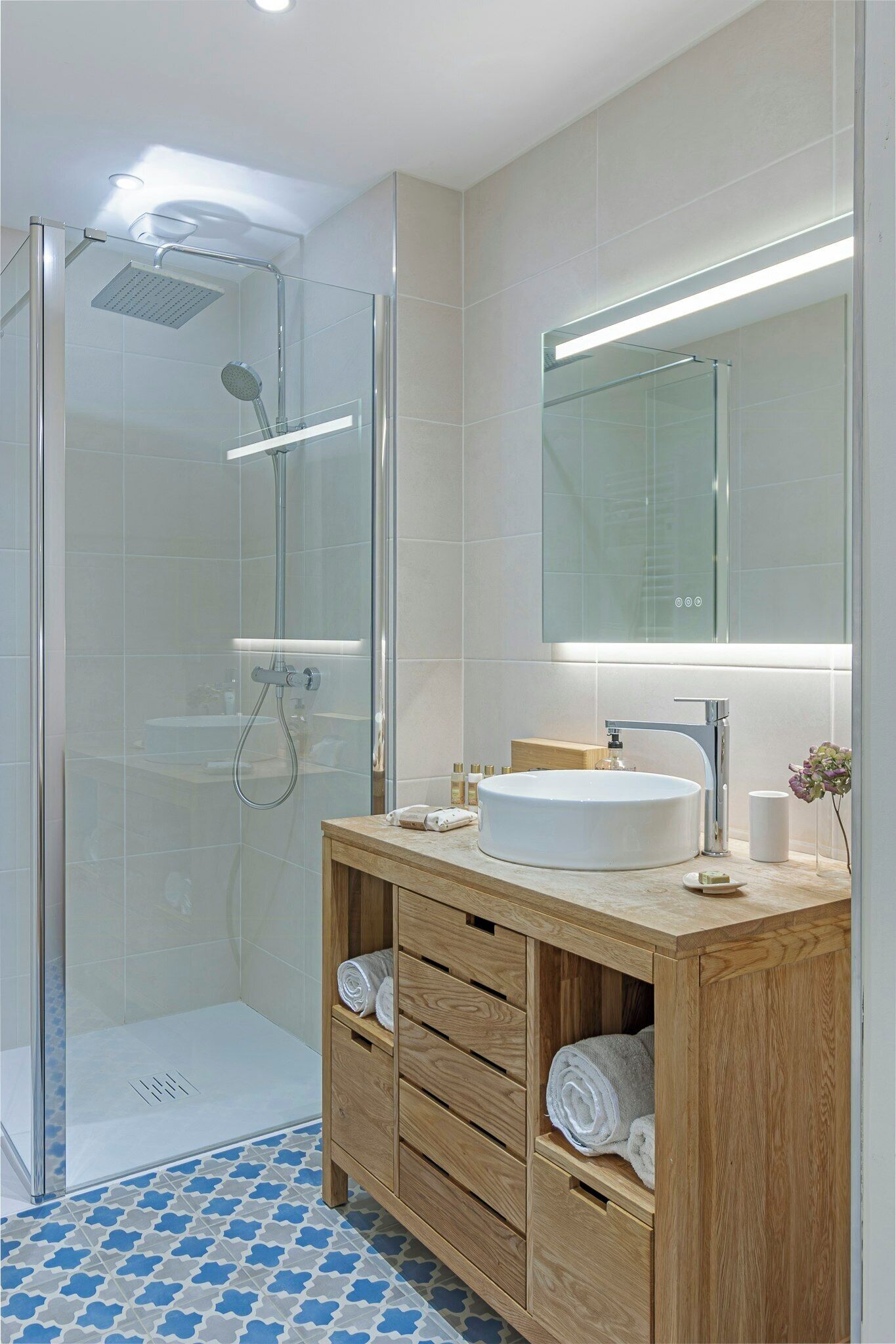Ein modernes Badezimmer mit einer Glaskabine zur Dusche, einem Holzwaschtisch mit Waschbecken und einem großen Spiegel.