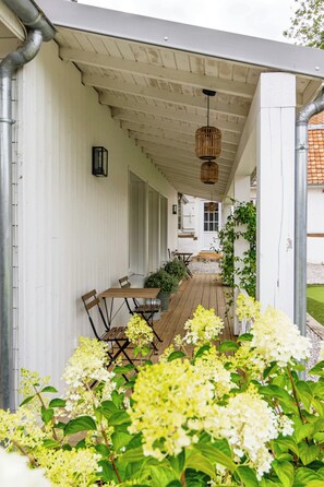 A covered outdoor seating area with wooden tables and chairs, surrounded by greenery and flowers. - 18th-century barn near Montreuil (Aix en Issart)