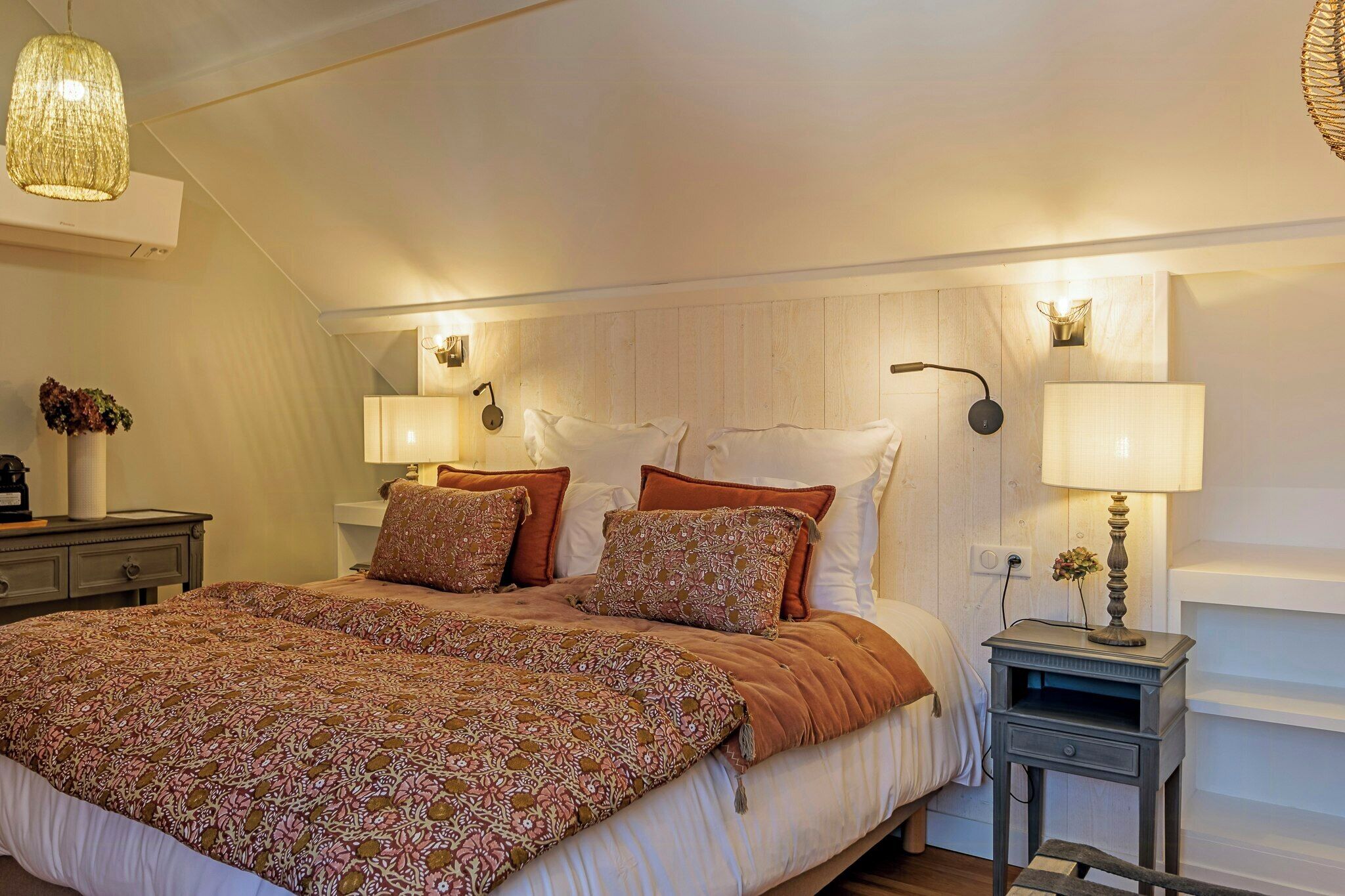 Een slaapkamer met een groot bed, twee bedlampen, een kleine tafel met lamp en een wandlamp.