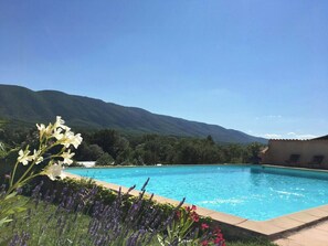 A swimming pool with a mountain backdrop, surrounded by lush greenery and flowers. - Provençal villa with Luberon views (Céreste-en-Luberon)