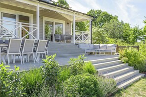 A covered outdoor seating area with chairs and a sofa, steps leading up to a building entrance, and surrounding greenery. - Modern holiday home with view and boat in Aspö (Drottningskär)