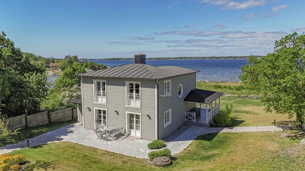 A two-story house with a patio, a deck, and a view of the water.