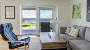 Una sala de estar con un sofá, un sillón, una mesa de centro y vista al mar a través de un ventanal.