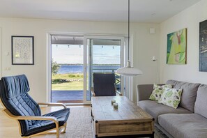 A living room with a sofa, a chair, a coffee table, and a view of the sea through a glass door. - Modern holiday home with view and boat in Aspö (Drottningskär)