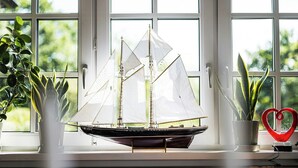 Un velero en miniatura sobre un alféizar, con plantas en macetas y una decoración con forma de corazón.