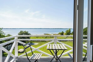 A balcony with a view of the sea, a wooden table, and a bench.