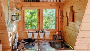 Une cuisine de taille réduite, équipée d’une cuisinière, d’un évier et d’une fenêtre donnant sur un espace verdoyant.