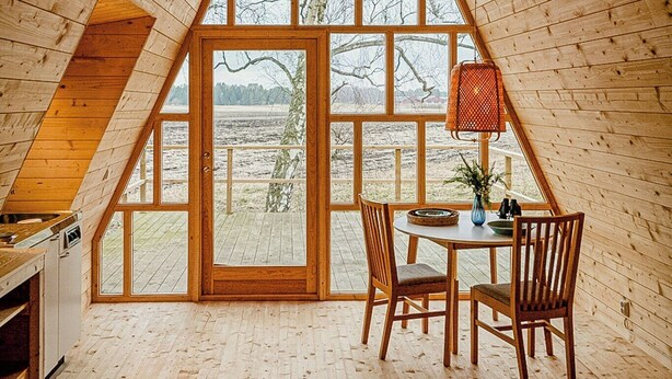 Une pièce aux murs en bois et au plafond incliné, avec une table à manger et des chaises, ainsi qu’une grande fenêtre.