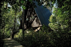 Eine Holzhütte mit geneigtem Dach, umgeben von dichtem Grün.