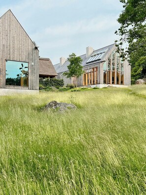 A modern building with large windows and a thatched-roof structure. - Designer farm with sauna by stream in Halland (Grimeton)