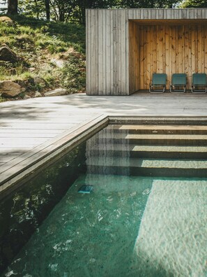 A swimming pool with a wooden deck and lounge chairs. - Designer farm with sauna by stream in Halland (Grimeton)