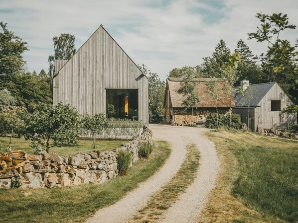A rural setting with a wooden barn, a stone wall, and a gravel path. - Designer farm with sauna by stream in Halland (Grimeton)