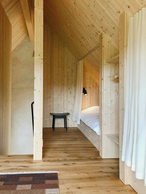 A wooden interior with a bed, a table, and a chair. - Designer farm with sauna by stream in Halland (Grimeton)