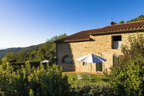 A stone building with a tiled roof, a small garden with a table and chairs, and a view of the hills. - Villa with pool in the heart of Chianti Rufina (Londa)