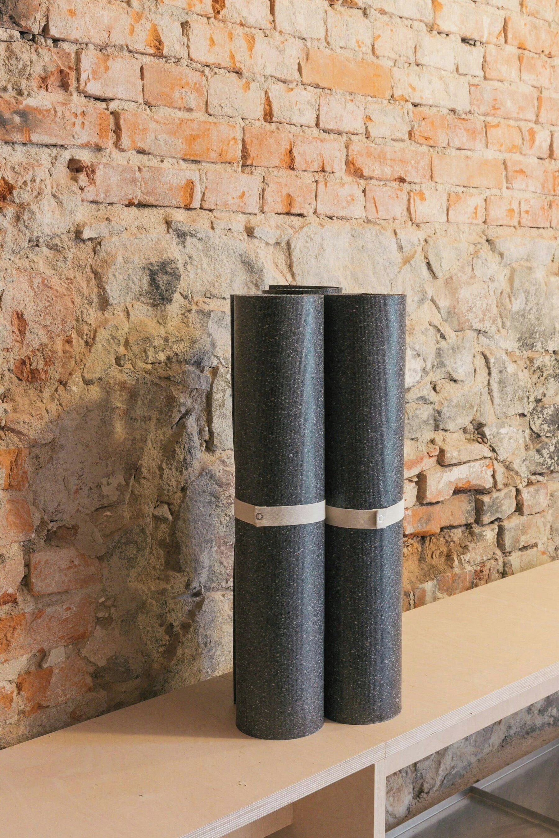 Two cylindrical objects with metal bands on a flat surface against a textured brick wall.