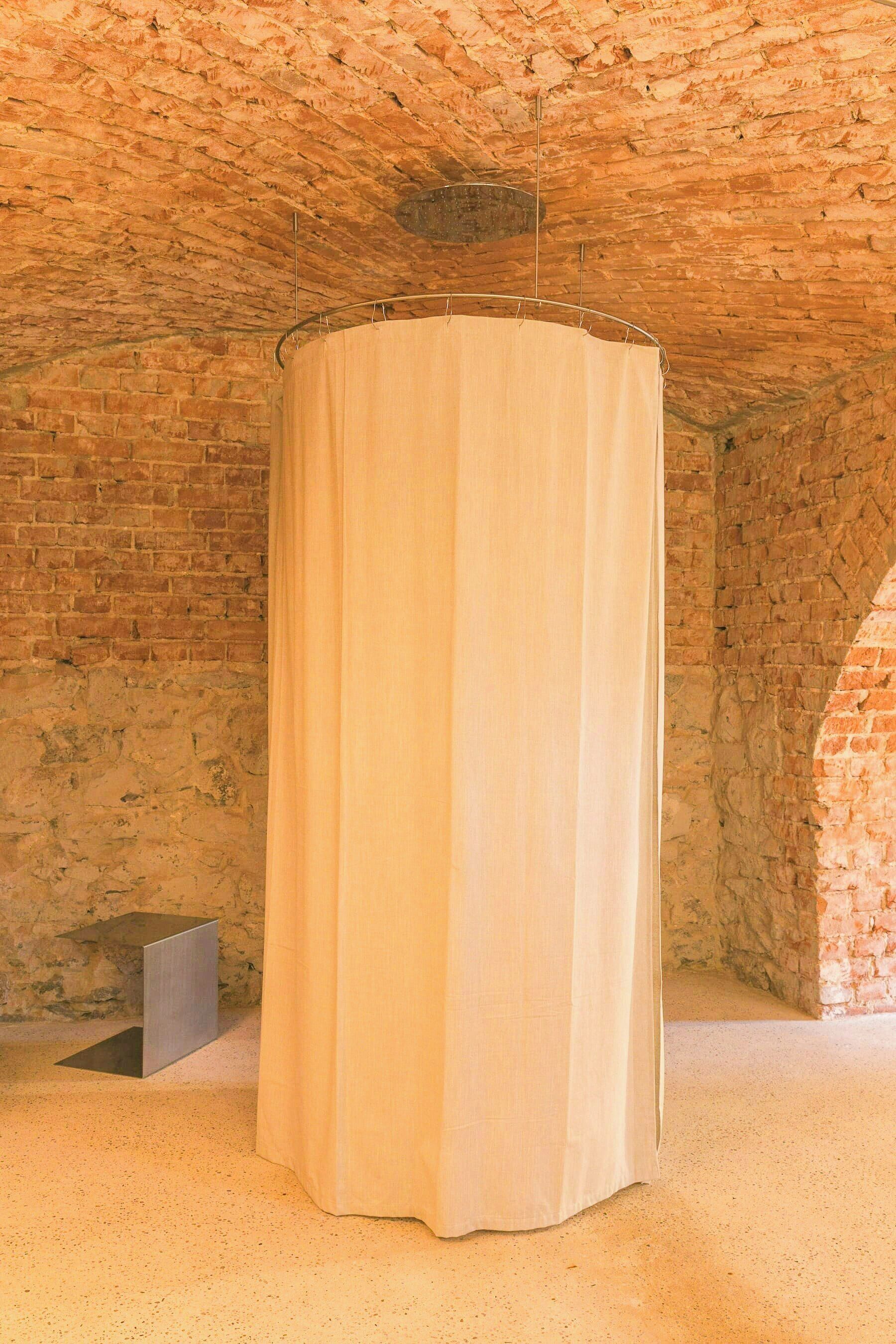 Una habitación con pared de ladrillo, cortina circular y un altavoz pequeño en el suelo.