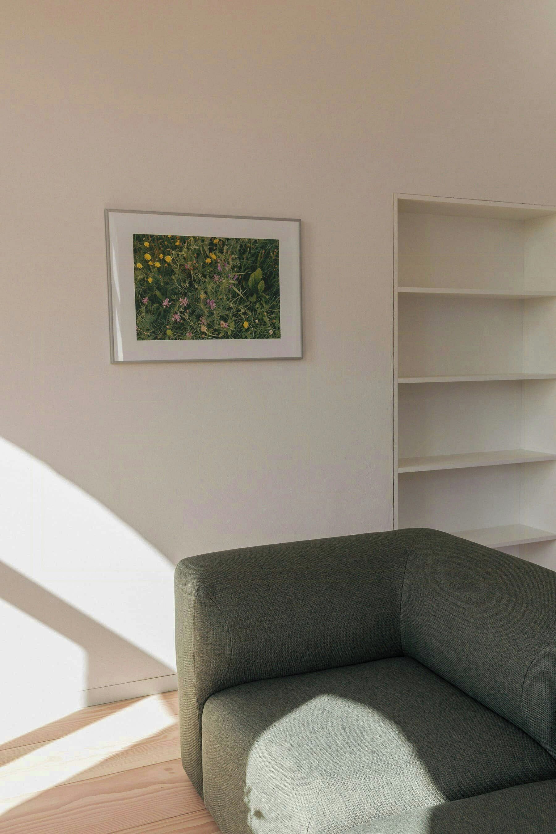 A room with a green sofa, a framed picture on the wall, and a white shelving unit.