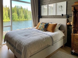 Un dormitorio con una cama grande, vista a un lago y obras de arte en la pared.