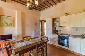 A dining area with a table set for two, a television, and a kitchen with white cabinets and a stove. - Your Oasis in the Heart of Tuscany (Montaione)