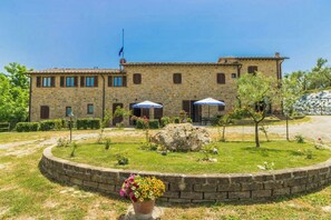 A stone building with a flag, a garden with a flower pot, and a paved area. - Your Oasis in the Heart of Tuscany (Montaione)