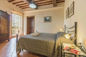 A bedroom with a bed, a nightstand with a lamp, a wardrobe, and a door leading to another room. - Your Oasis in the Heart of Tuscany (Montaione)