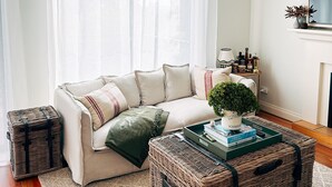 A living room with a sofa, two wicker baskets, a small table with books, and a potted plant. - Premium 2 Bedroom French Villa + Free Wine Tasting (Pokolbin)