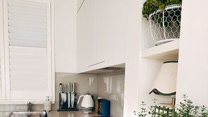 A modern kitchen with white cabinetry, a black countertop, and a potted plant on the right. - Premium 2 Bedroom French Villa + Free Wine Tasting (Pokolbin)
