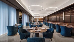 A modern hotel dining area with round tables, blue upholstered chairs, and a long counter. - Crystal Orange Hotel Shenzhen Bay MixC (Shenzhen)