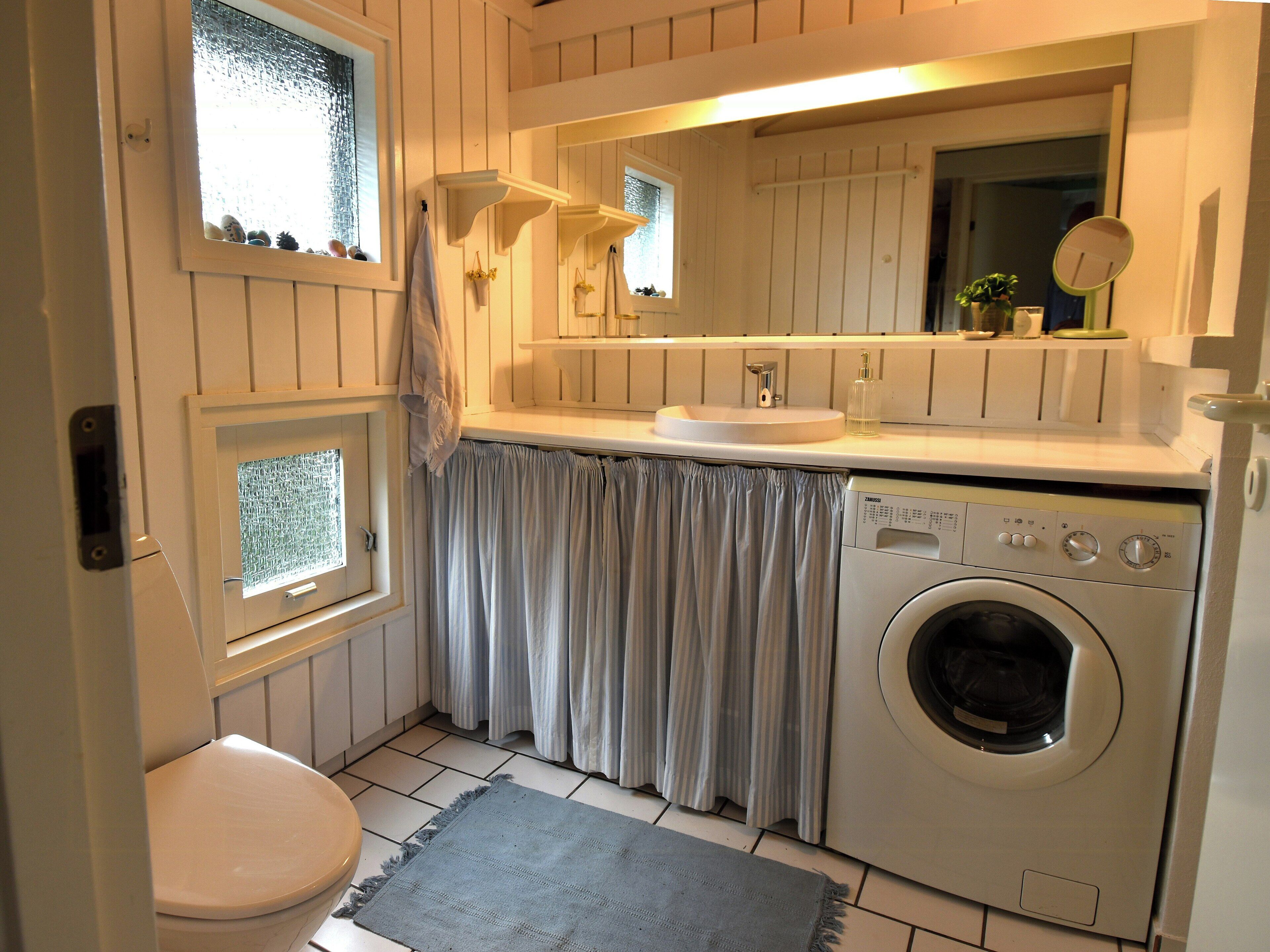 Une petite salle de bain comprenant des toilettes, un lave-linge et une fenêtre avec des rideaux.