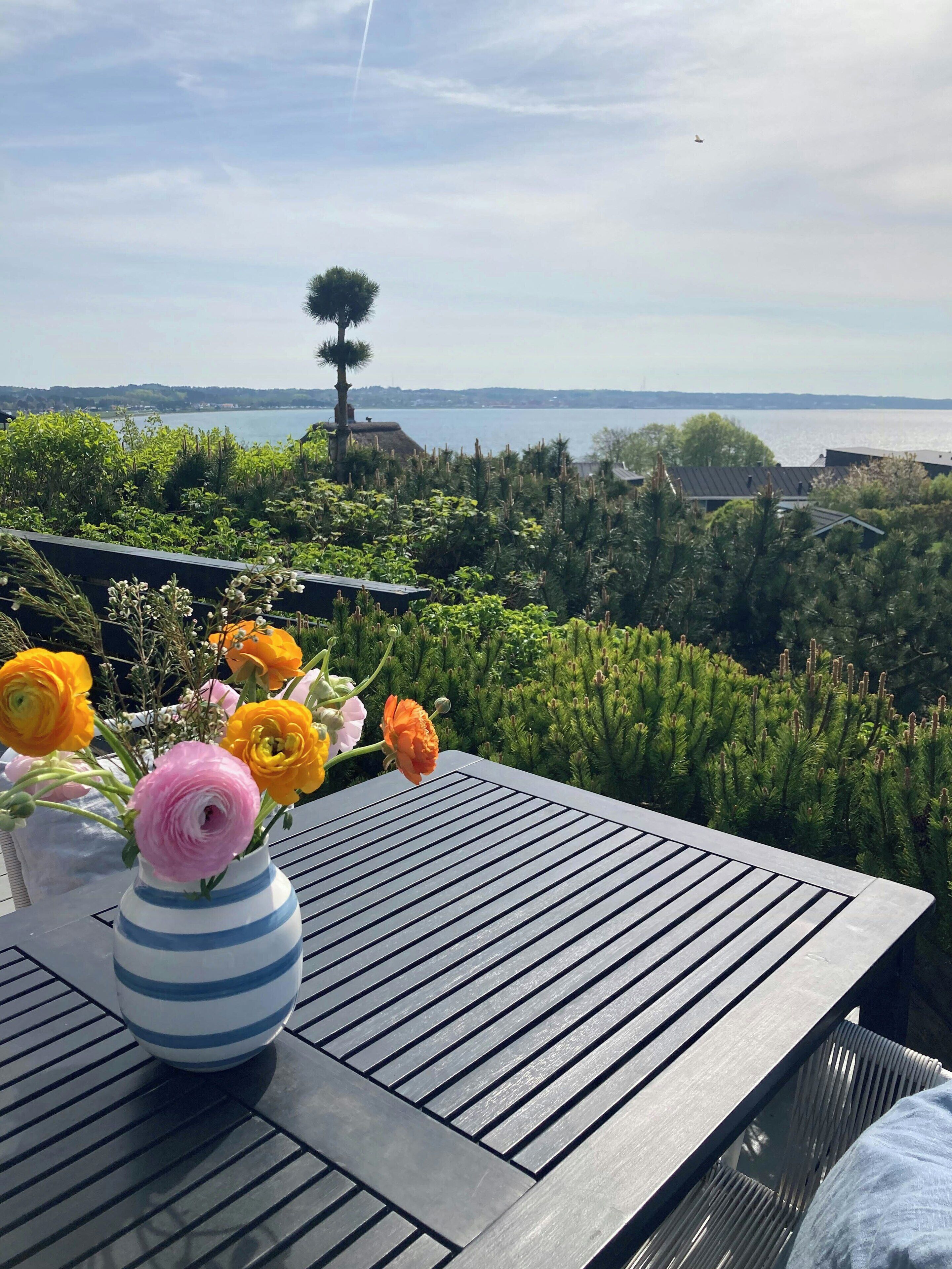 Une table ornée d’un vase de fleurs, avec vue sur une étendue d’eau et sur la végétation environnante.