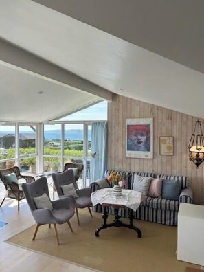 Ein modernes Wohnzimmer mit einer Couch, Sesseln, einem Tisch und Blick durch große Fenster.