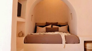 Un dormitorio con cama, almohadas y mesita de noche.