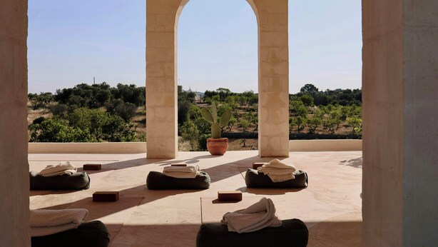Una terraza con pilares de piedra, una planta en maceta y varios cojines.