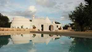 Un edificio blanco con piscina frente a él, rodeado de cactus y árboles.