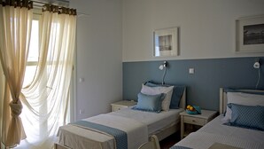 Ein Schlafzimmer mit zwei Betten, einem Nachttisch, einem Stuhl und einem Fenster mit durchsichtigen Vorhängen.