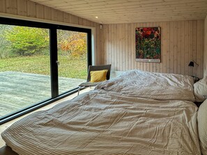 Ein Schlafzimmer mit einem großen Bett, einem Sessel, einem Gemälde und Blick auf einen Garten durch eine Schiebetür.