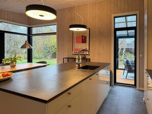 Eine moderne Küche mit einer großen Kochinsel, Pendelleuchten und Blick ins Freie.