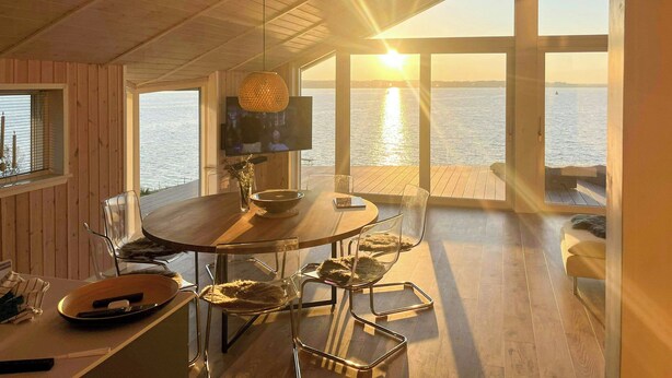 Un comedor con mesa de madera, sillas, televisor y vista al mar.