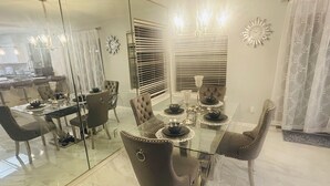 Een eetruimte met een glazen tafel, donkere fauteuils en een moderne kroonluchter.