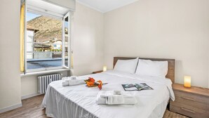 Una camera d'albergo con un letto grande, una finestra vista montagna e acqua, un comodino con una lampada e un termosifone.