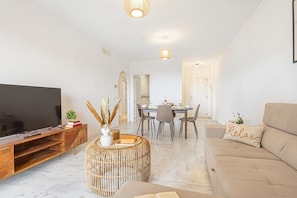 A living room with a TV, sofa, dining table, and chairs.