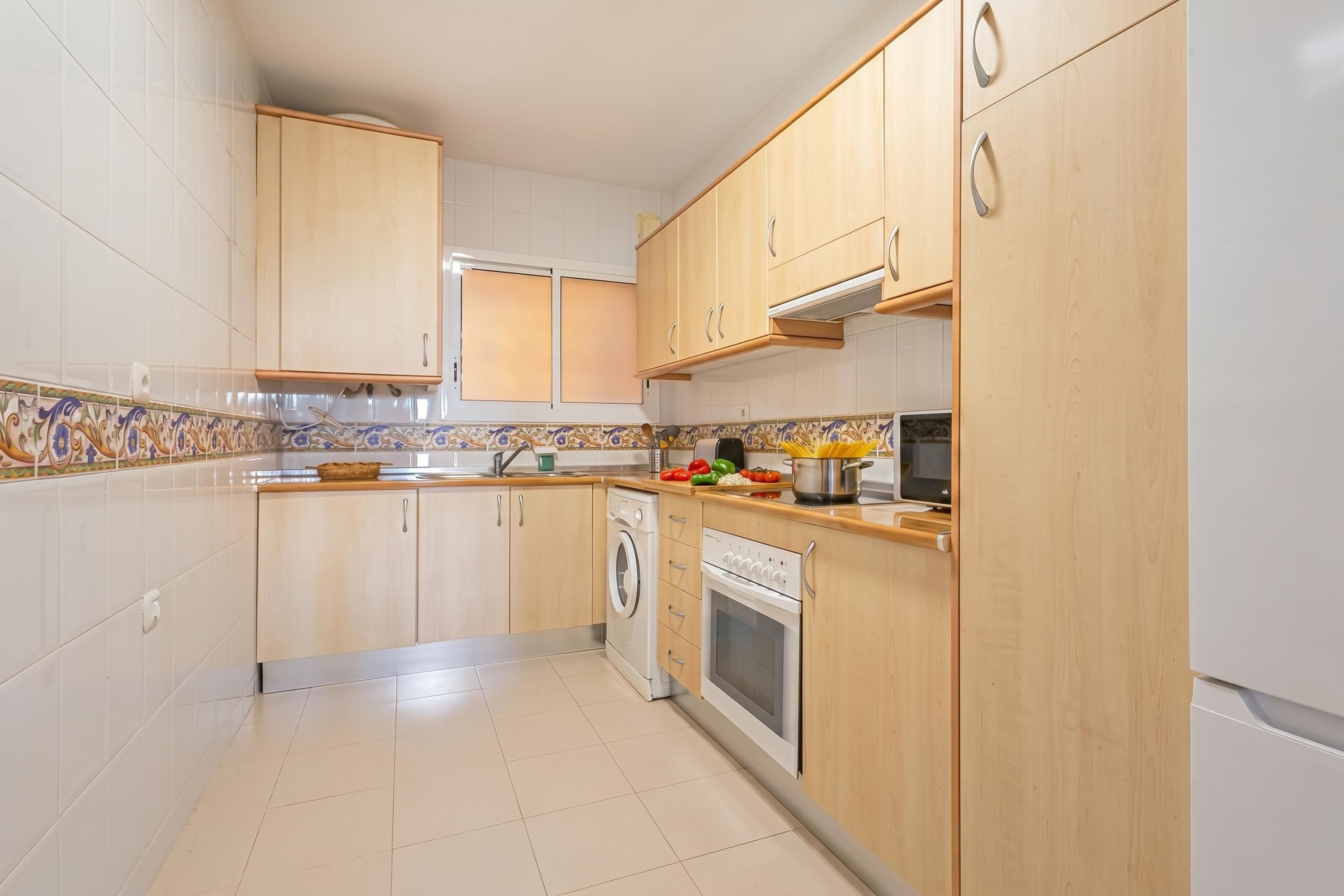 A kitchen with wooden cabinets, a washing machine, an oven, and a microwave.