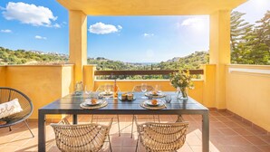 Un balcon avec une table dressée pour le dîner, des chaises en osier et une vue sur le paysage.
