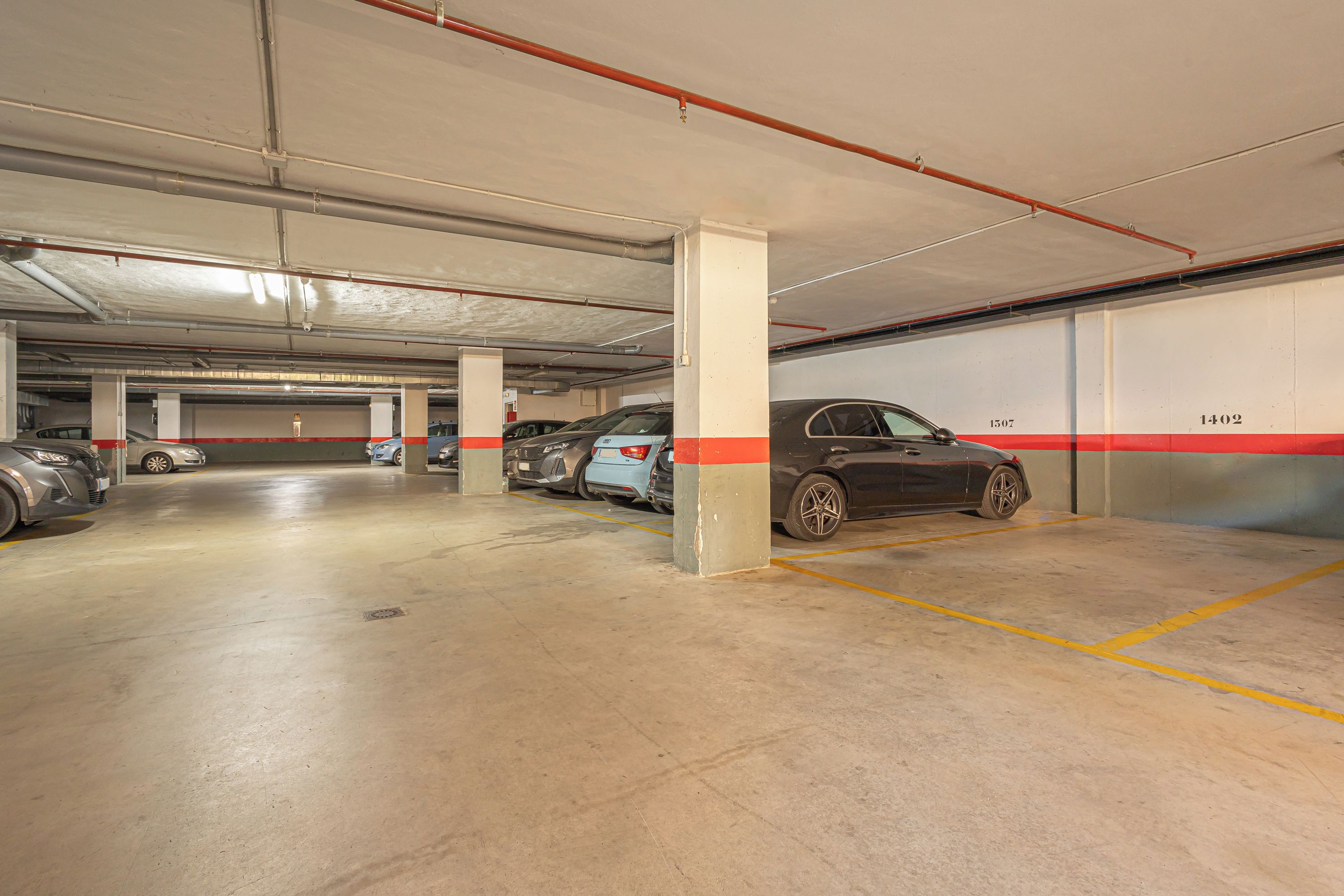 Un estacionamiento subterráneo de varios niveles con pisos de concreto, pilares y espacios de estacionamiento delimitados.