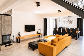 A modern living room with a fireplace, sofa, TV, dining area, and staircase. - Villa Anastazija Family Retreat With Pool (Sveta Nedelja)