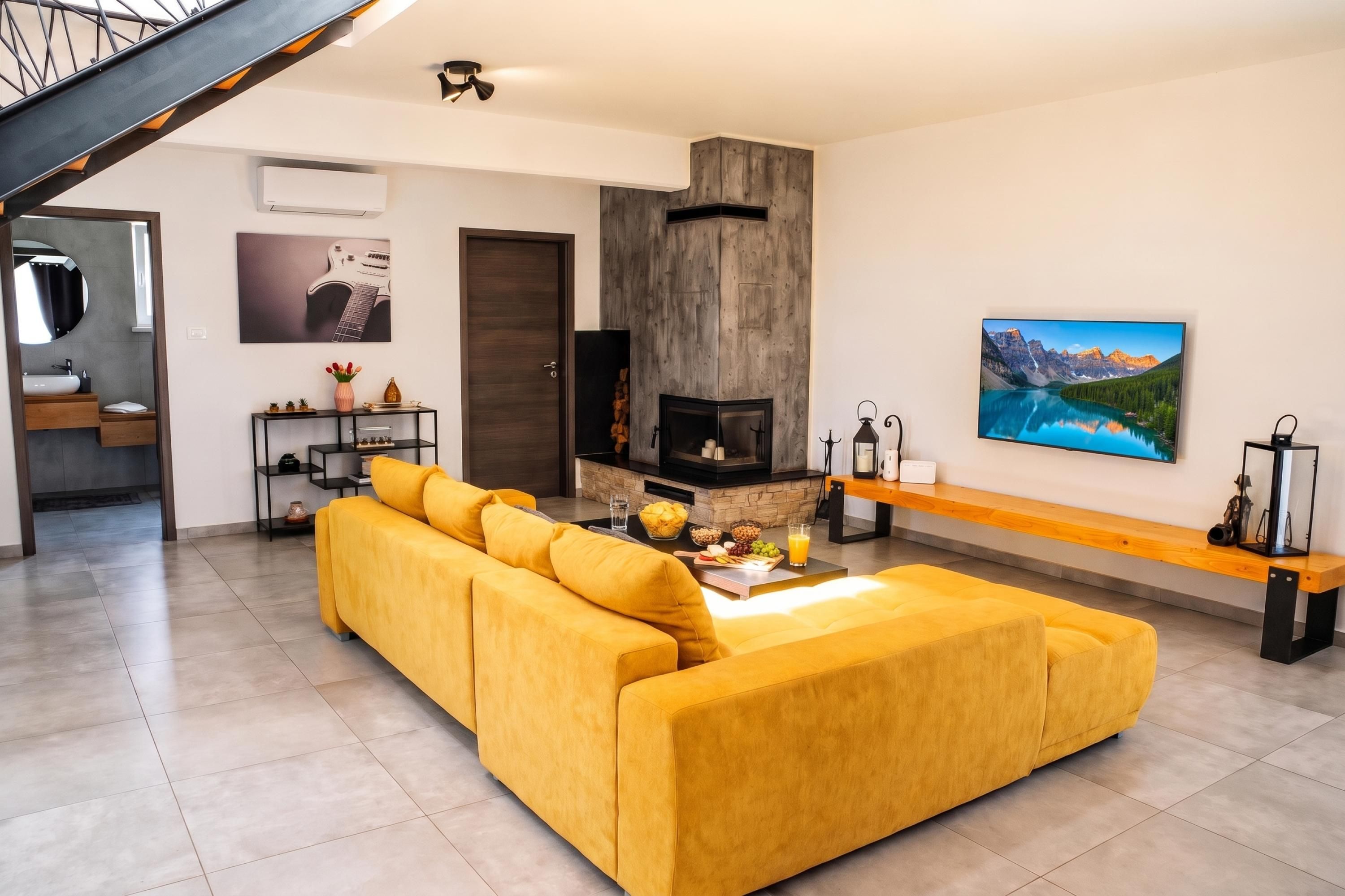 A modern living room with a yellow sofa, a fireplace, and a large landscape painting.