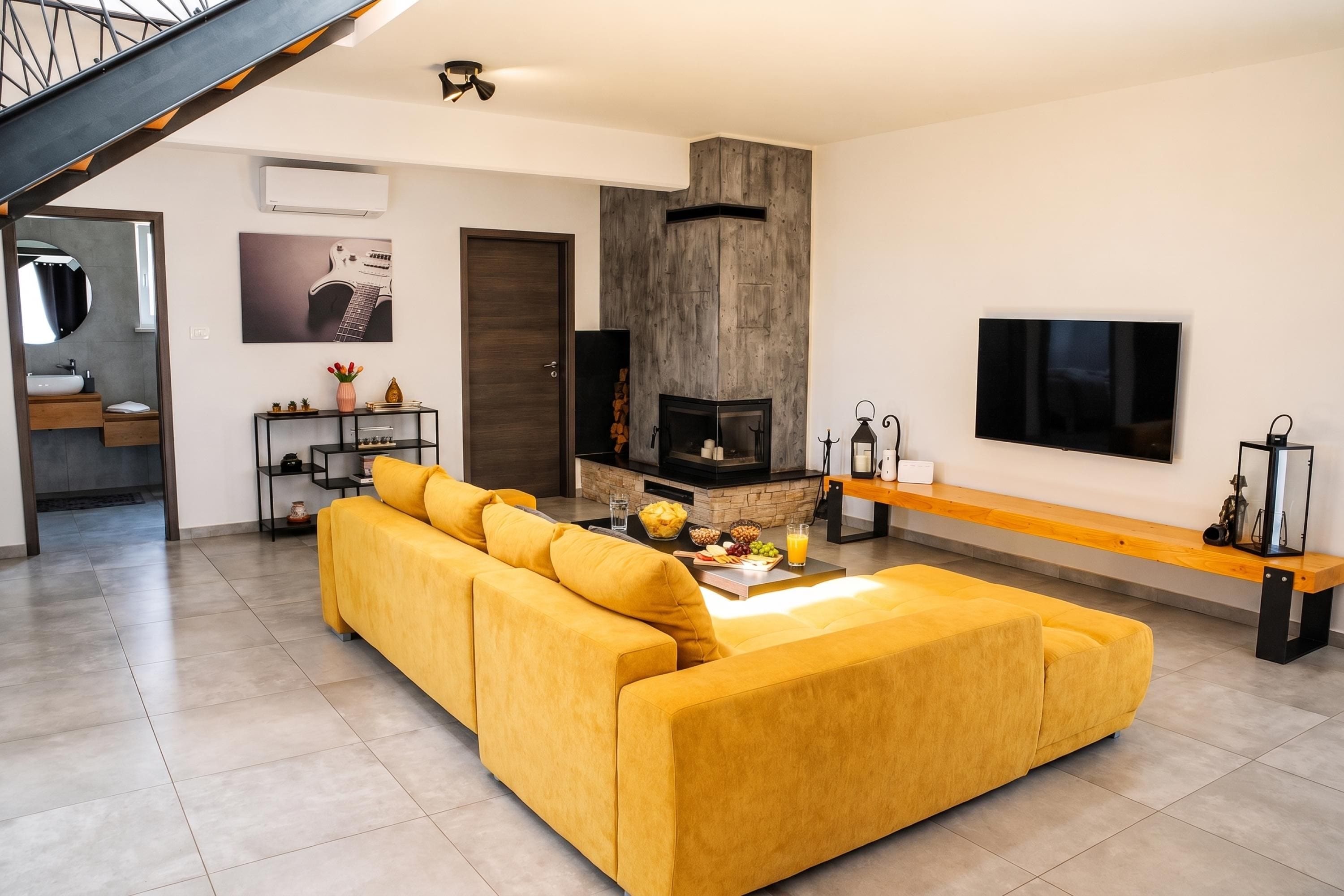 A modern living room with a sofa, a fireplace, a TV, and a staircase.