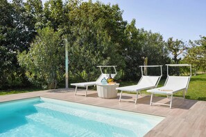 Ein Swimmingpool mit zwei weißen Liegestühlen und einem runden Tisch mit Vase und Buch.